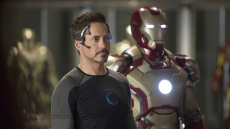 Homem de Ferro | Saiba a ordem cronológica dos filmes de Tony Stark no MCU Tony Stark, interpretado por Robert Downey Jr., aparece em primeiro plano usando traje tecnológico enquanto a armadura do Homem de Ferro está posicionada atrás dele em laboratório futurista.