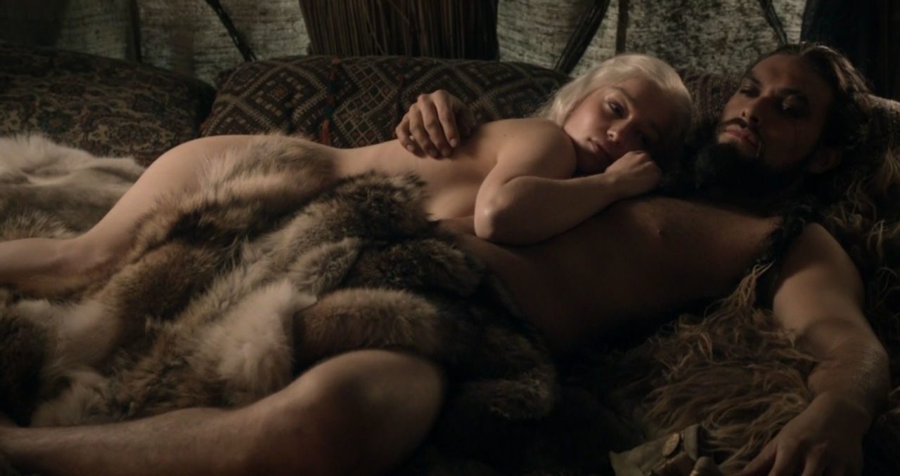 Emilia Clarke e Jason Momoa  aparecem deitados em uma cama com seus corpos nus semi cobertos por peles de animal em uma de suas muitas cenas quentes em Game of Thrones