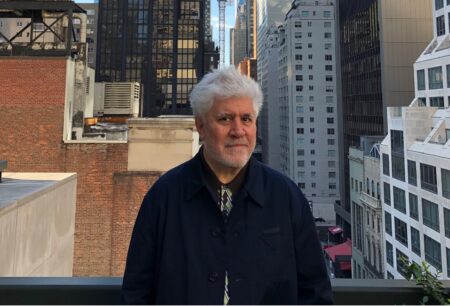 O cineasta Pedro Almodóvar posando para uma foto com altos prédios ao fundo!