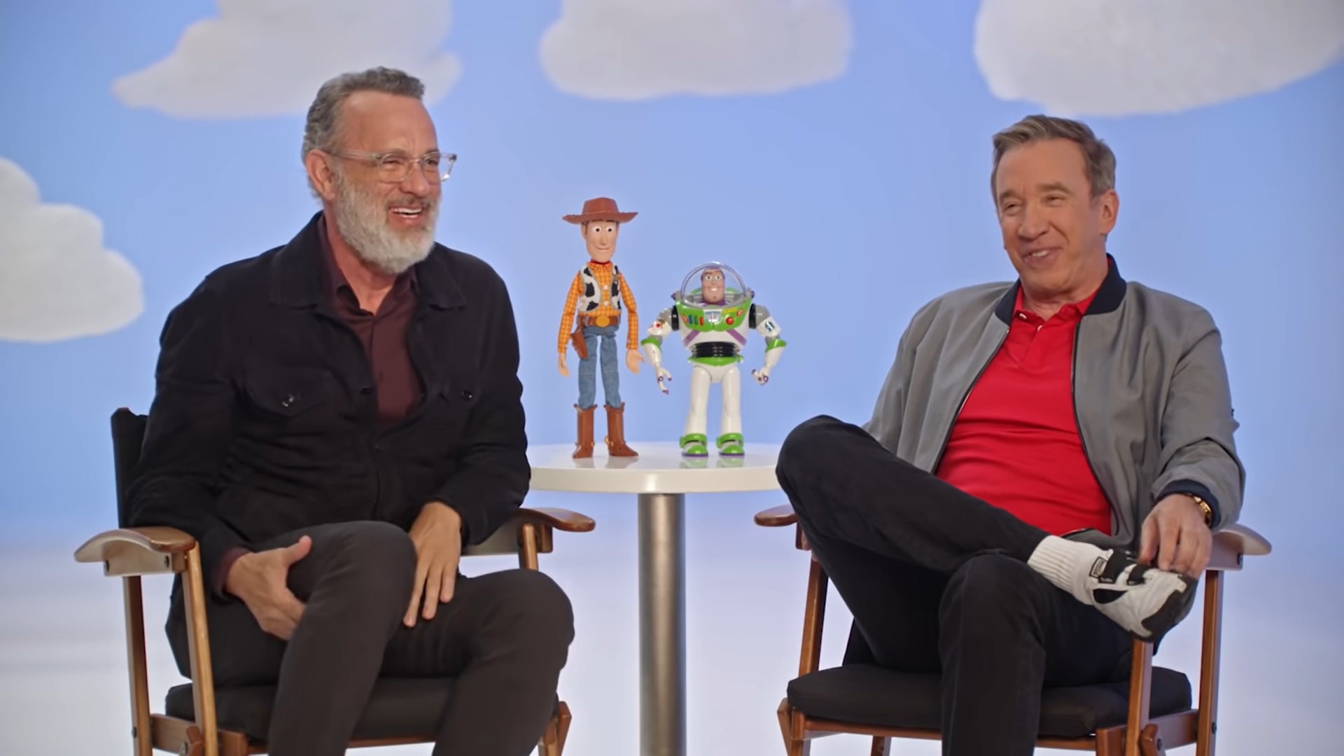 Tom Hanks e Tim Allen sentados aos lados de bonecos de seus personagens em entrevista com a Pixar sobre a franquia Toy Story