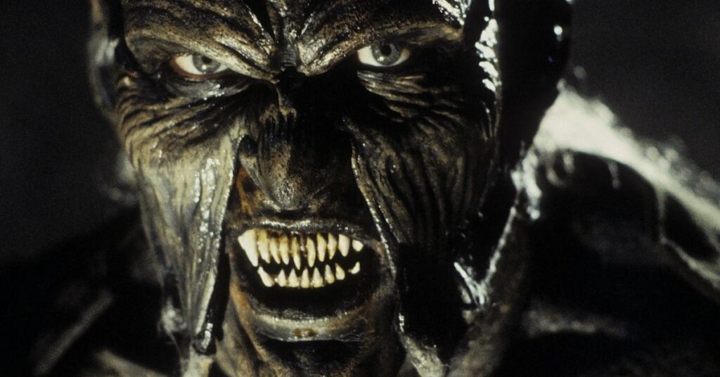 Olhos Famintos: a verdadeira história de origem e segredos do Creeper Close do rosto do Creeper mostrando dentes afiados e pele enrugada no filme Olhos Famintos, destacando o visual monstruoso da criatura.