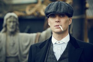 Peaky Blinders retorna com sequência e duas novas temporadas já confirmadas Cillian Murphy interpretando Thomas Shelby em Peaky Blinders, usando boina escura, sobretudo preto e cigarro na boca, com estátua religiosa desfocada ao fundo.