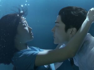 Cena subaquática do dorama Extraordinary You (2019), mostrando Eun Dan-oh (Kim Hye-yoon) desmaiada na piscina enquanto Ha-ru (Rowoon) a segura nos braços, prestes a salvá-la, em um momento simbólico de conexão entre os personagens.