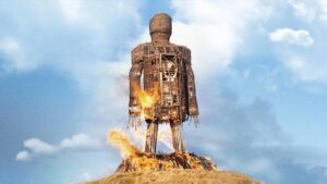 Imensa escultura humana feita de palha queimada sob o céu azul em cena icônica de The Wicker Man (1973), simbolizando o sacrifício ritual do terror folk britânico.