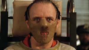 Close-up do personagem usando uma máscara de contenção no filme O Silêncio dos Inocentes (1991), com olhar fixo e intenso.