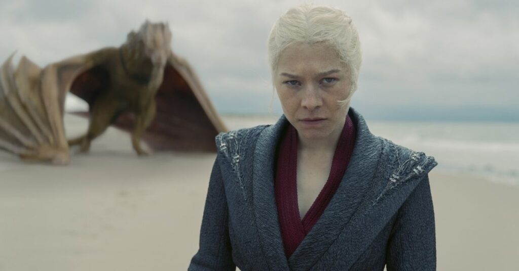 Rhaenyra Targaryen caminha na praia enquanto seu dragão aparece ao fundo em cena de A Casa do Dragão