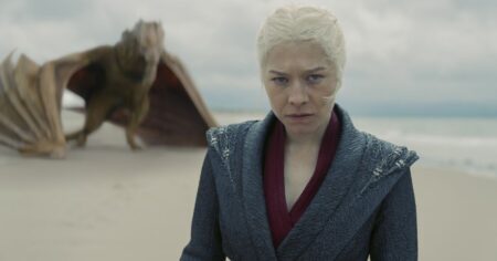 Rhaenyra Targaryen caminha na praia enquanto seu dragão aparece ao fundo em cena de A Casa do Dragão
