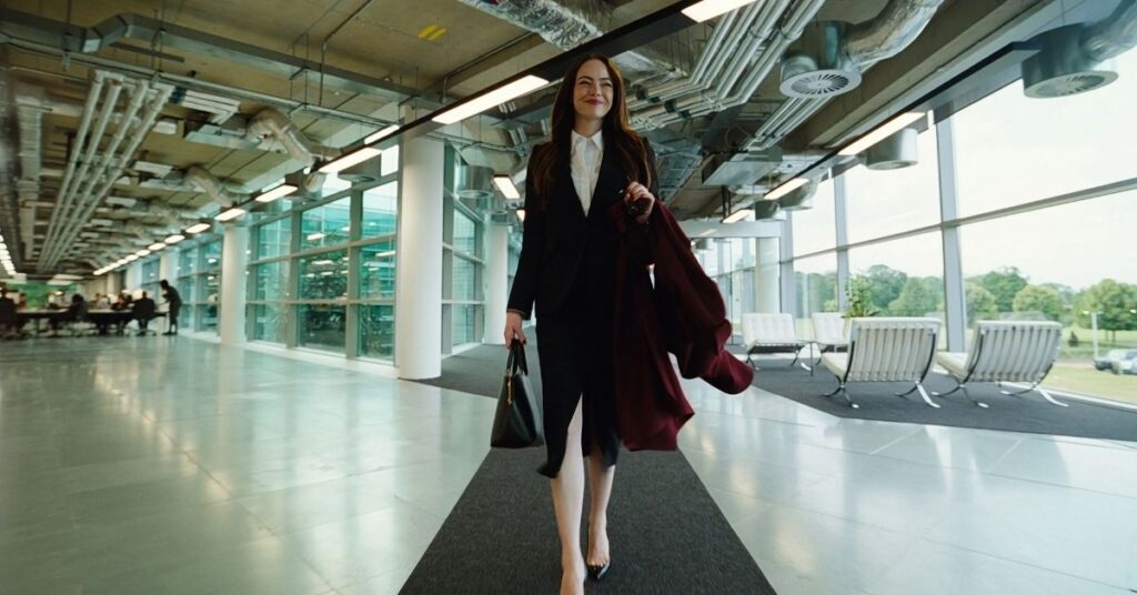 Cena de Bugonia mostra personagem caminhando por corredor corporativo com bolsa e casaco, um dos lançamentos da semana no cinema