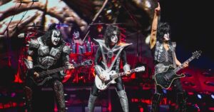 Membros do KISS se apresentam no palco com figurinos clássicos e maquiagem marcante durante show de rock.