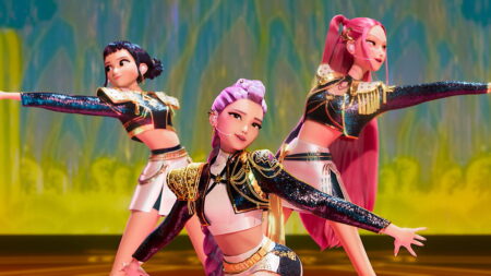 As integrantes do grupo HUNTR/X, Rumi, Mira e Zoey, se apresentam em um palco colorido com figurinos brilhantes e coreografia sincronizada.