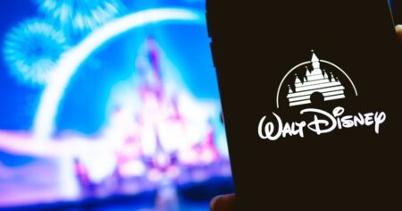 Logotipo da Disney exibido na tela de um smartphone, com castelo iluminado e fogos de artifício ao fundo, simbolizando o estúdio e o entretenimento cinematográfico global.