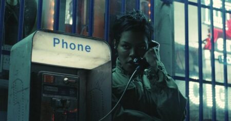 Cinema em 2025: 8 atrizes que tiveram atuações marcantes Teyana Taylor em cena de Uma Batalha Após a Outra, usando um telefone público em ambiente urbano noturno com atmosfera tensa e iluminação fria