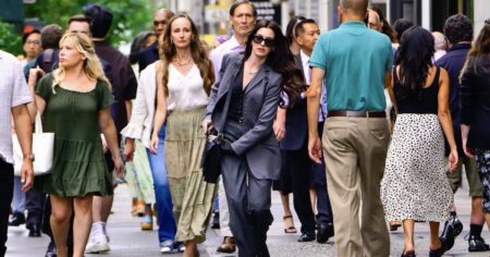 Duna 3, Dia D e mais: os 20 filmes mais aguardados de 2026 Grupo de pessoas caminha por uma rua movimentada da cidade, com destaque para uma mulher de terno cinza e óculos escuros em meio a pedestres vestidos de forma elegante.