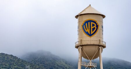 Warner Bros rejeita oferta da Paramount e critica riscos financeiros Torre de água com o logotipo da Warner Bros em estúdio da empresa, cercada por montanhas sob céu nublado, representando a Warner Bros Discovery em Los Angeles