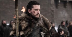 Kit Harington caracterizado como Jon Snow em cena de batalha da série Game of Thrones, usando armadura escura e manto de pele em ambiente medieval coberto de neve