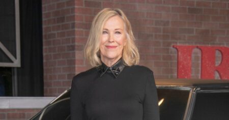 Catherine O’Hara posa para fotógrafos em evento de cinema, usando vestido preto, diante de carro clássico