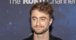 Daniel Radcliffe esclarece boato sobre Wolverine no MCU; entenda Daniel Radcliffe em evento de divulgação com fundo azul e expressão séria