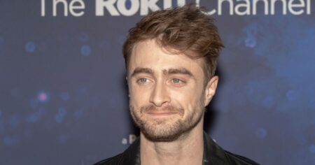 Daniel Radcliffe em evento de divulgação com fundo azul e expressão séria