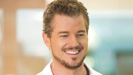 Close em Eric Dane sorrindo, com barba aparada e cabelo curto levemente grisalho, em ambiente interno com fundo desfocado.