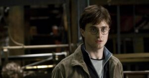 Harry Potter: Daniel Radcliffe faz apelo aos fãs sobre nova série Daniel Radcliffe como Harry Potter em cena do filme da Warner Bros., usando óculos redondos e expressão séria dentro de Hogwarts