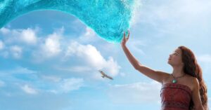 Personagem Moana estende a mão em direção a uma onda de água azul em cena do live-action, com o céu aberto ao fundo