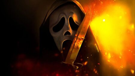 Pânico 7 amarga no Rotten Tomatoes e tem a pior nota da franquia; entenda Ghostface aparece em close, usando manto preto com capuz e a máscara branca de expressão alongada. Ele segura uma faca refletindo chamas, enquanto o fundo é iluminado por fogo intenso e faíscas, criando atmosfera dramática e ameaçadora