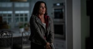 Pânico 7: trailer do Super Bowl sela destino de Sidney Prescott Neve Campbell, como Sidney Prescott, segura uma arma com expressão de alerta em uma cozinha clara durante cena de Pânico 7.