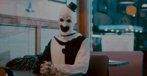 Art the Clown sentado em lanchonete com maquiagem branca e chapéu preto em cena de Terrifier 4