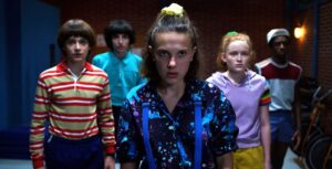 Grupo de adolescentes liderados por Eleven caminhando em clima de tensão em Hawkins, cena que reforça por que vale a pena assistir Stranger Things para quem gosta de suspense e amizade.