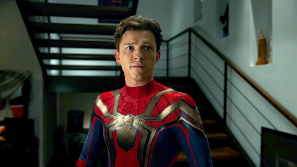 Tom Holland aparece usando o traje do Homem-Aranha dentro de uma casa, com expressão preocupada, diante de uma escada moderna ao fundo.