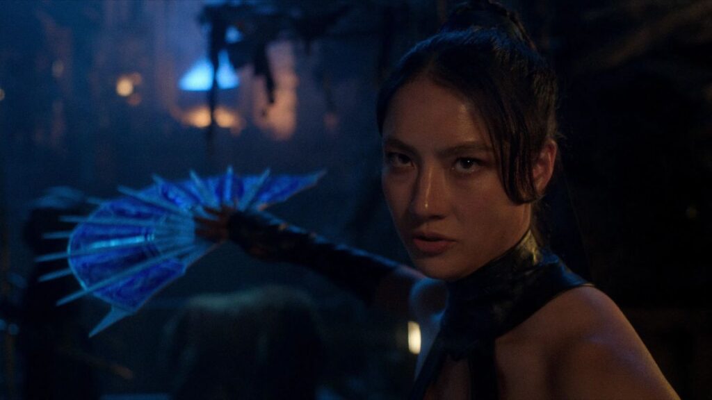 Adeline Rudolph interpretando Kitana em cena de Mortal Kombat 2 vestida com uniforme azul da personagem e mostrando o leque.