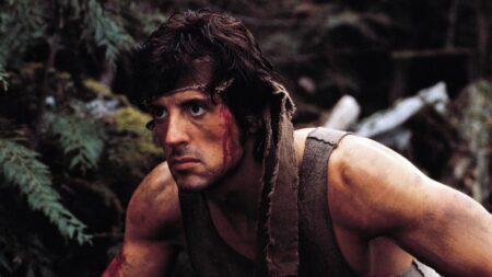 Sylvester Stallone aparece caracterizado como o personagem John Rambo, com aparência ferida e suja em meio à floresta.