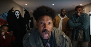 Todo Mundo em Pânico 6: Marlon Wayans quer fim da cultura do cancelamento Marlon Wayans como o personagem Shorty Meeks em Todo Mundo em Pânico 6, aparecendo em primeiro plano com expressão de choque e boca aberta, enquanto o vilão Ghostface e outros personagens aparecem ao fundo em um cenário interno.