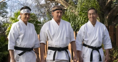 Cobra Kai temporada 7 - Daniel LaRusso, Johnny Lawrence e Chozen Toguchi vestindo quimonos brancos e faixas pretas durante cena da temporada final de Cobra Kai ao ar livre
