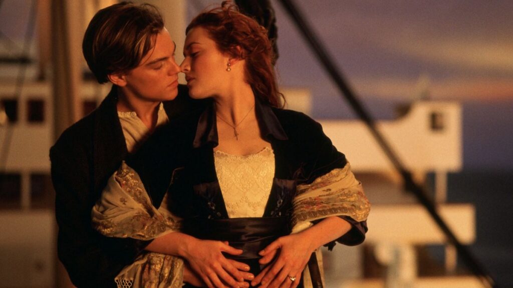 Filmes de romance: 30 histórias apaixonantes para assistir e se emocionar Cena romântica do filme Titanic mostra um casal abraçado no convés de um navio ao pôr do sol, com clima íntimo e expressão de paixão
