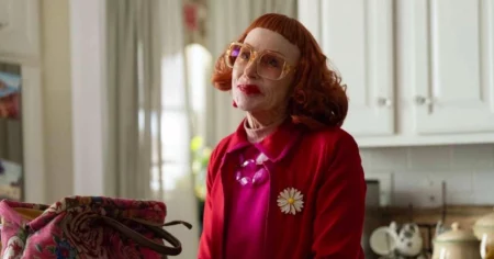 Gladys: prelúdio de A Hora do Mal ganha data e explora origem da bruxa Amy Madigan caracterizada como Gladys em cena de filme, com cabelo ruivo, óculos grandes e figurino vermelho em ambiente doméstico