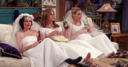 Atriz de ‘Friends’ expõe fortuna anual do elenco; veja valores Três personagens de Friends aparecem sentadas em um sofá, vestidas de noiva, enquanto assistem à televisão em cena da sitcom
