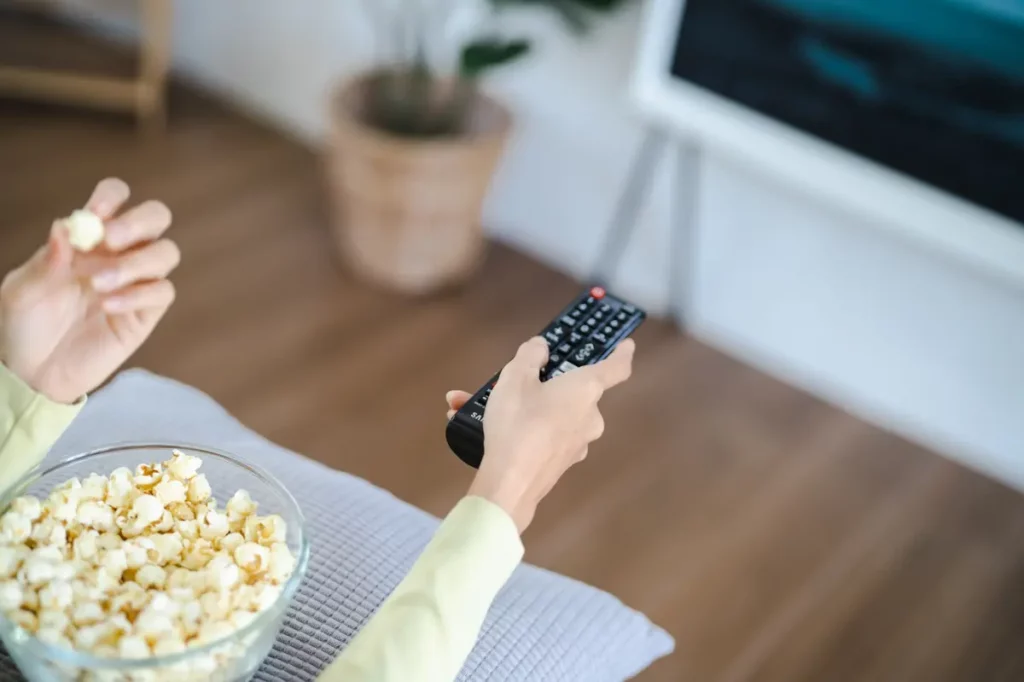Melhor streaming: compare os principais serviços para assistir filmes e séries no Brasil Pessoa assistindo TV com pipoca em casa, representando o uso do melhor streaming para ver filmes e séries no Brasil