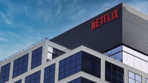 Netflix recua e pode levar mais filmes aos cinemas após reuniões com gigantes do setor, diz site Fachada moderna do prédio da Netflix com logotipo vermelho em destaque no topo, céu azul ao fundo e arquitetura corporativa contemporânea