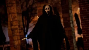 Pessoa usando máscara de Ghostface segurando uma faca em um ambiente escuro, com iluminação urbana ao fundo, remetendo a cenas de suspense e terror.