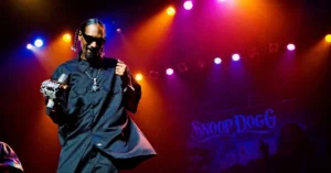 Snoop Dogg confirma produção de cinebiografia sobre sua carreira Snoop Dogg se apresenta no palco com microfone durante show, destacando carreira do rapper tema de cinebiografia