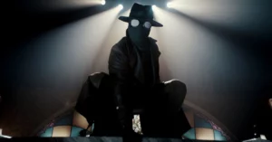 Nicolas Cage caracterizado como Spider-Noir com traje escuro, máscara e chapéu sob luz dramática em ambiente inspirado nos anos 1930