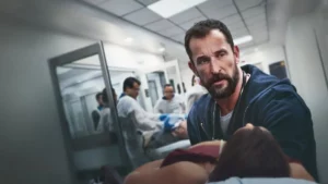 Arte promocional de The Pitt mostrando um médico em um atendimento tenso.