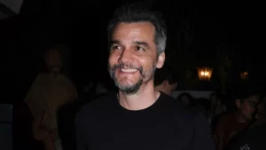 Wagner Moura entra para a lista de 100 pessoas mais influentes no mundo; entenda o motivo Wagner Moura sorrindo em evento noturno, usando camiseta preta, com público e iluminação ao fundo