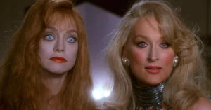 Goldie Hawn e Meryl Streep aparecem lado a lado em cena de A Morte Lhe Cai Bem, com figurinos glamourosos e expressão séria