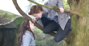 Crepúsculo assistir online: onde ver a saga completa, ordem e qualidade Cena romântica de Bella e Edward em Crepúsculo assistir online, com Edward em uma árvore olhando para Bella
