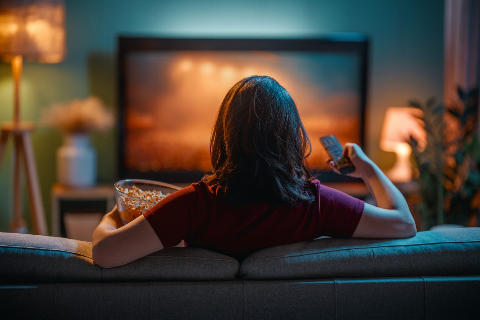 Melhores séries para assistir: 50 opções imperdíveis para maratonar agora Mulher sentada no sofá, com balde de pipoca vendo séries
