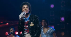 Jaafar Jackson interpreta Michael Jackson durante apresentação musical no filme Michael, usando figurino brilhante e segurando um microfone no palco.