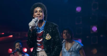 Jaafar Jackson interpreta Michael Jackson durante apresentação musical no filme Michael, usando figurino brilhante e segurando um microfone no palco.