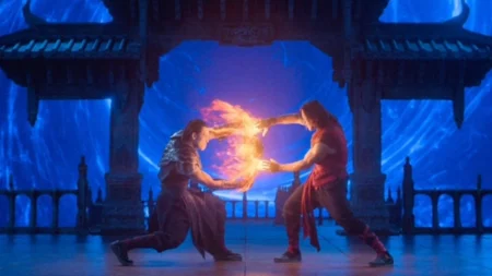 Mortal Kombat 2: bastidores revelam como luta entre Baraka e Cage ganha forma Dois personagens se enfrentando com poderes de fogo em um cenário azul com estrutura oriental ao fundo no ambiente do filme Mortal Kombat 2
